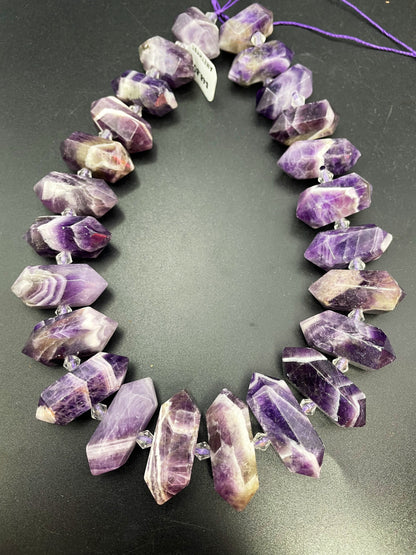 AAA Natural Amethyst stone bead. 12x26-12x34mm graduated barrel shape. Gorgeous natural purple color with white lines. Full strand 15.5”